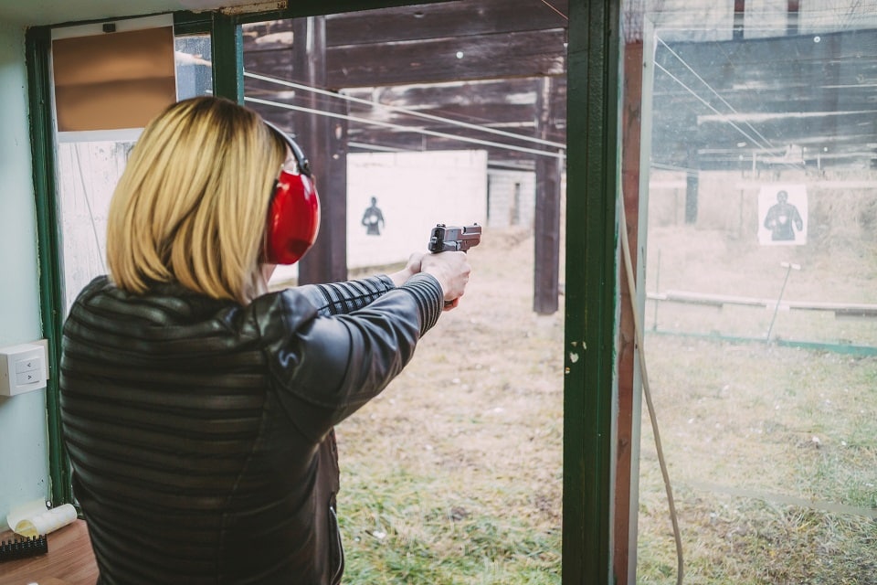 female trainee wearing hearing protection and firing a handgun at an outdoor gun range