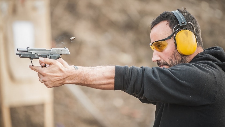 man firing pistol at gun range, wearing ear protection