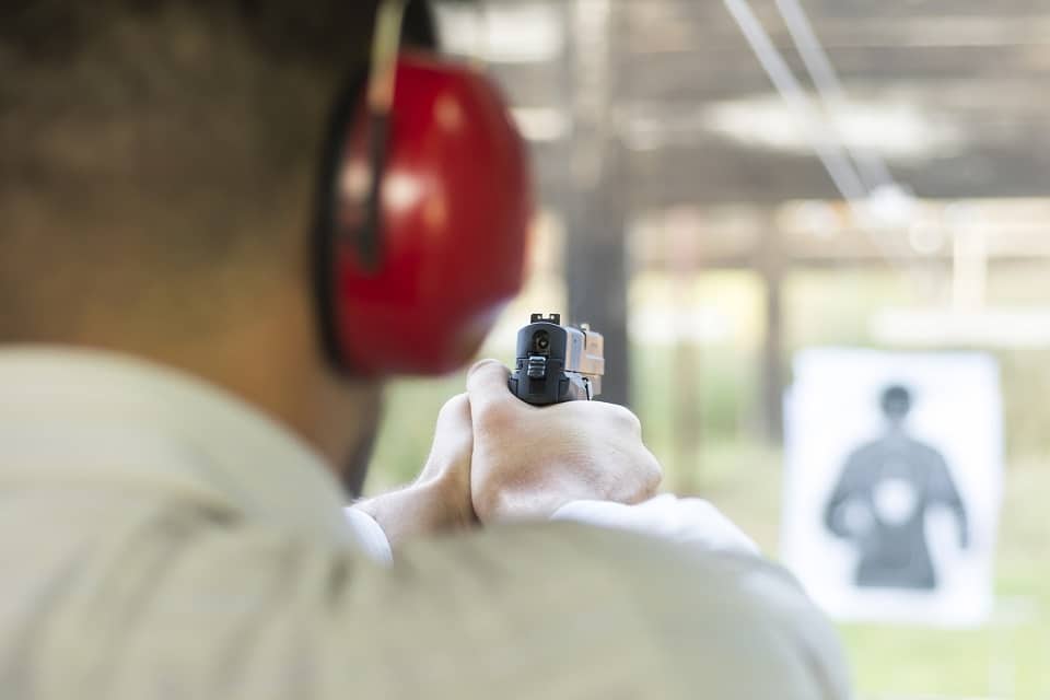 trainee wearing hearing protection and firing a handgun at an outdoor gun range
