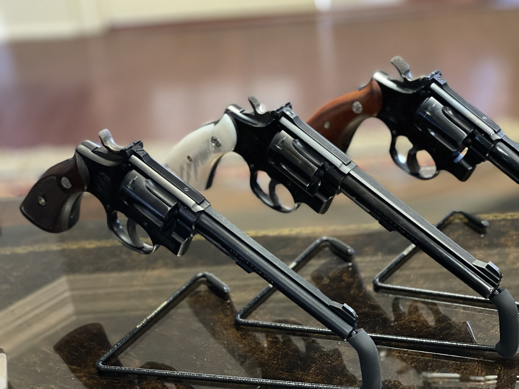 Three blued Smith & Wesson K-Frame revolvers displayed on stands with adjustable sights, long barrels, and mixed walnut and pearl stocks