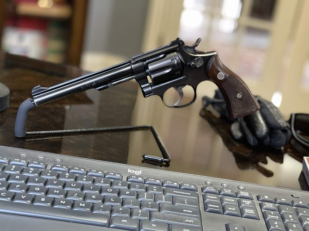 Blued Smith & Wesson K-Frame revolver with long barrel, adjustable rear sight, exposed hammer, and checkered walnut medallion stocks displayed on a desk